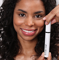 Une femme affiche avec confiance un tube de mascara, présentant son produit de beauté avec un sourire éclatant.