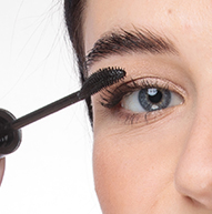 Une femme applique du mascara avec un pinceau, ajoutant du volume à ses cils et perfectionnant le maquillage de ses yeux.