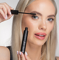 Une femme applique soigneusement du mascara sur ses cils, en tenant la brosse de près pour une finition parfaite.