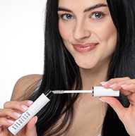 Une femme tient élégamment un tube de mascara Nanolash, mettant en valeur sa beauté et sa confiance dans un cadre élégant.