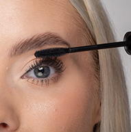 Une femme utilise une brosse à mascara pour appliquer le mascara, rehaussant habilement ses cils pour une apparence plus dramatique.