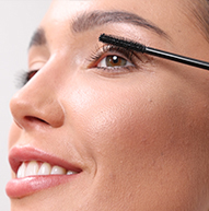 On voit une femme appliquer du mascara avec une brosse, rehaussant soigneusement ses cils pour une apparence plus dramatique.