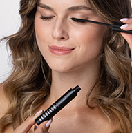 Une femme applique soigneusement du mascara pour rehausser ses cils, en se concentrant attentivement sur sa routine de maquillage.