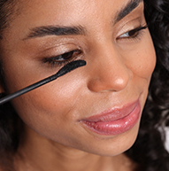 Une femme applique du mascara sur ses yeux, présentant son processus de maquillage dans un environnement lumineux et élégant.