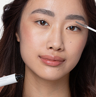 Une femme se concentre sur l’application du maquillage avec un pinceau, mettant en valeur son talent artistique et son processus de soins personnels.