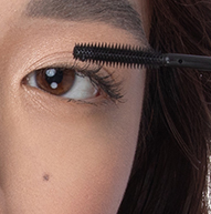 On voit une femme appliquer du mascara avec une brosse, en se concentrant sur ses cils pour obtenir un look défini et élégant.